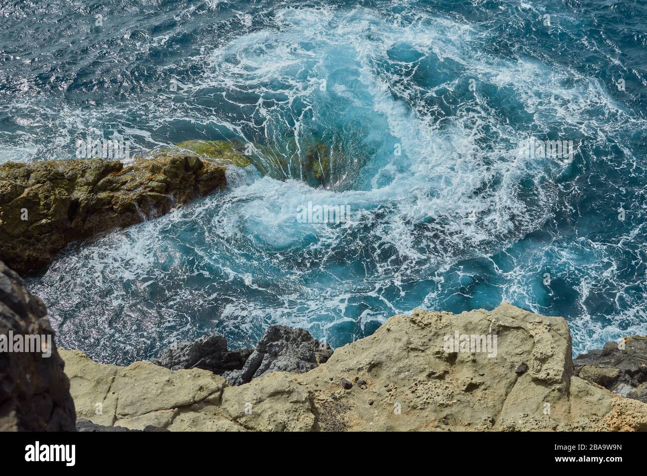 Vortice naturale con schiuma nel mare di ​​the villaggio di Ajuy visto dalla cima della gola di formazione rocciosa a Fuerteventura, Isole Canarie, Spagna Foto Stock