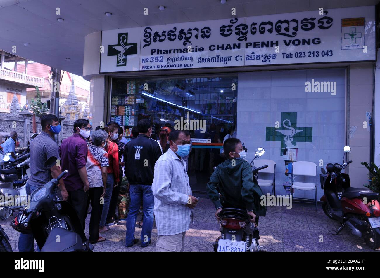 Cambogiani, indossando maschere facciali, attendere in linea fuori da una farmacia per acquistare farmaci durante la pandemia coronavirus, Phnom Penh, Cambogia. © Kraig Lieb Foto Stock