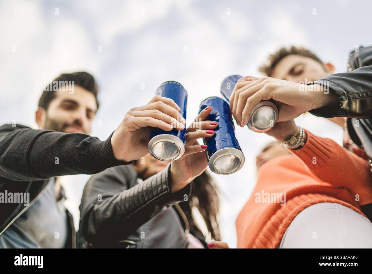 I giovani amici tostano con birre in scatola. Mettere a fuoco la lattina, i volti sfocati. Foto Stock