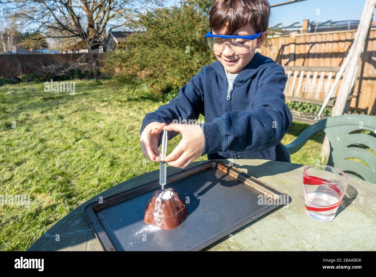 Un ragazzo fa un esperimento scientifico nel giardino mescolando aceto e bicarbonato di soda per simulare un'eruzione vulcanica. Foto Stock