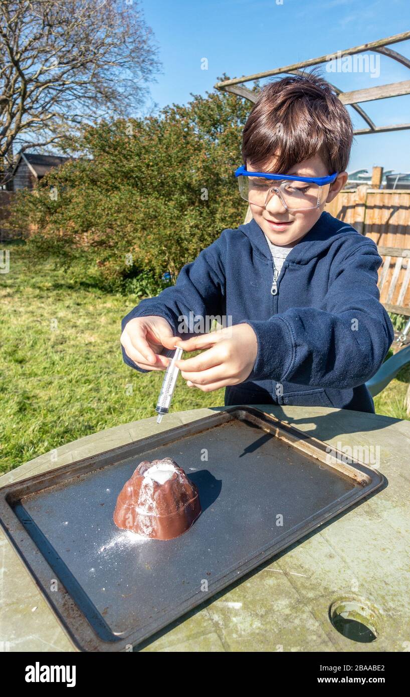 Un ragazzo fa un esperimento scientifico nel giardino mescolando aceto e bicarbonato di soda per simulare un'eruzione vulcanica. Foto Stock