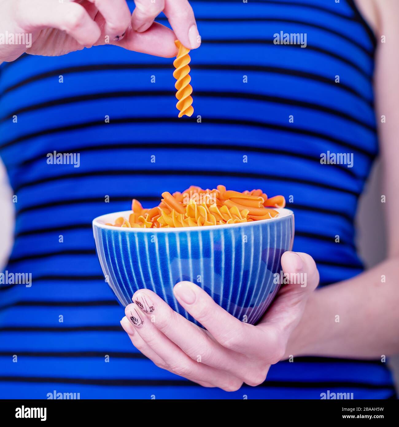 Ciotola per mani femminili con lenticchie di arancia fusilli su fondo a righe blu. Concetto di dieta e senza glutine Foto Stock