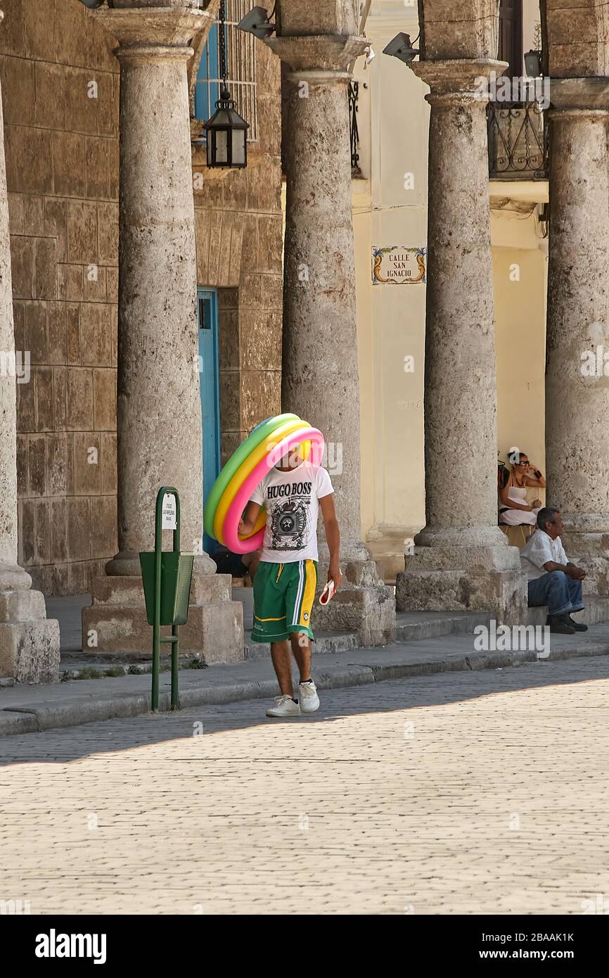 Giovane uomo cubano che cammina e trasporta una piscina gonfiabile multicolore sulla sua testa in Plaza Vieja a l'Avana Foto Stock