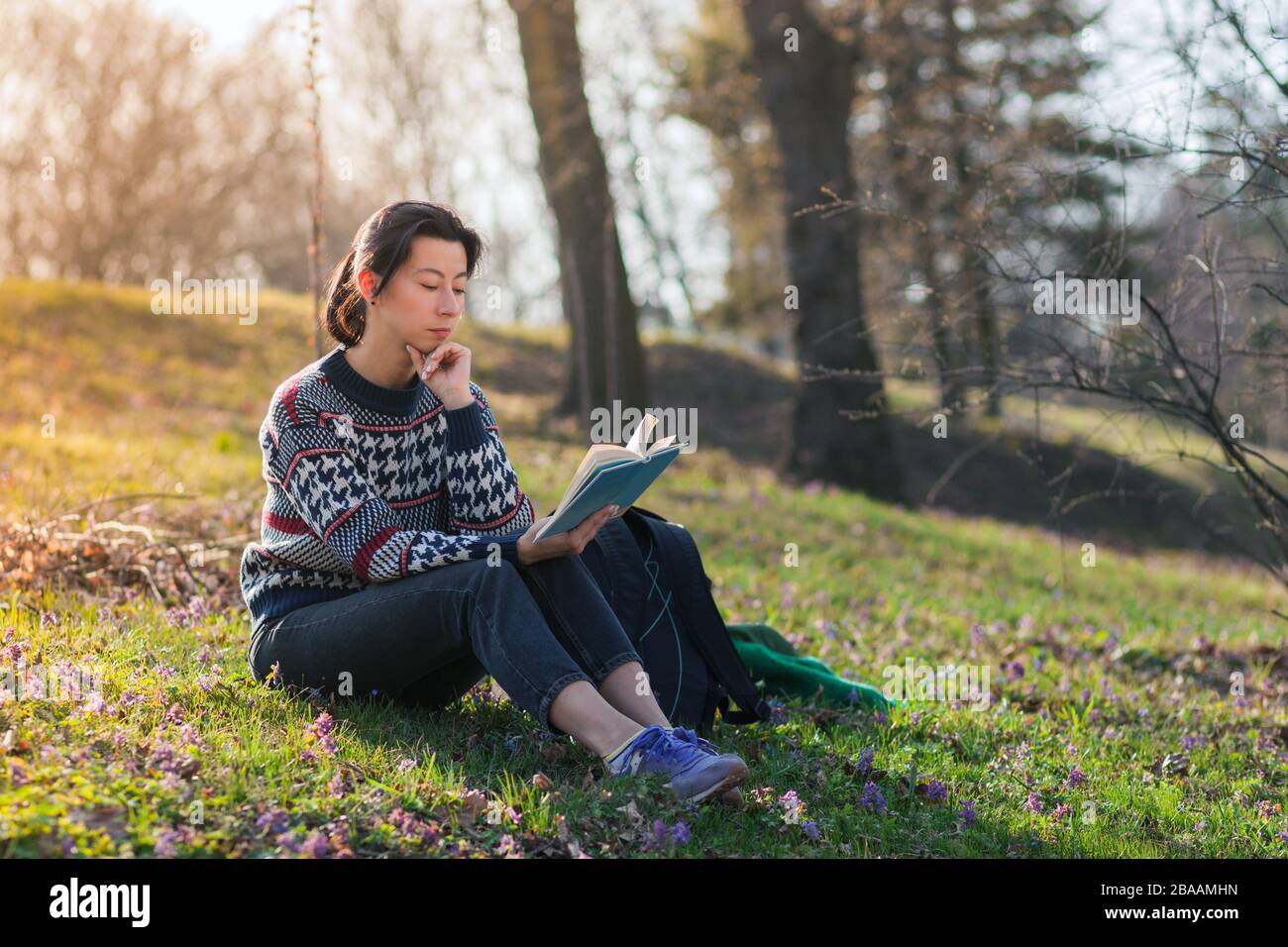 Bella ragazza bruna è seduta sull'erba nel parco e leggere un libro. All'aperto in primavera o autunno. Foto Stock