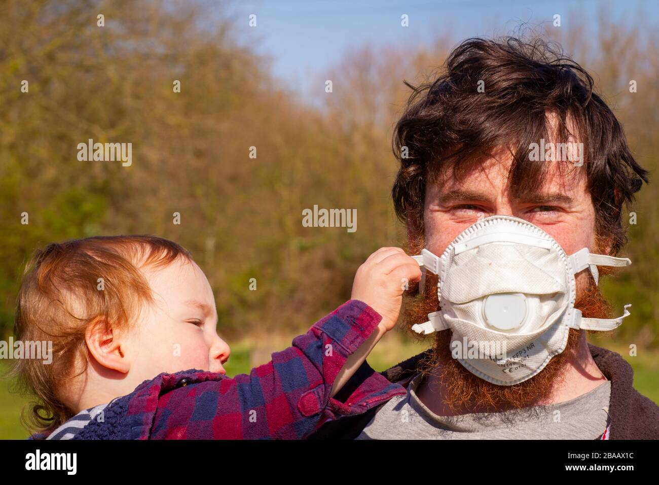 Padre con facemask e bambino cercando di rimuoverlo Foto Stock