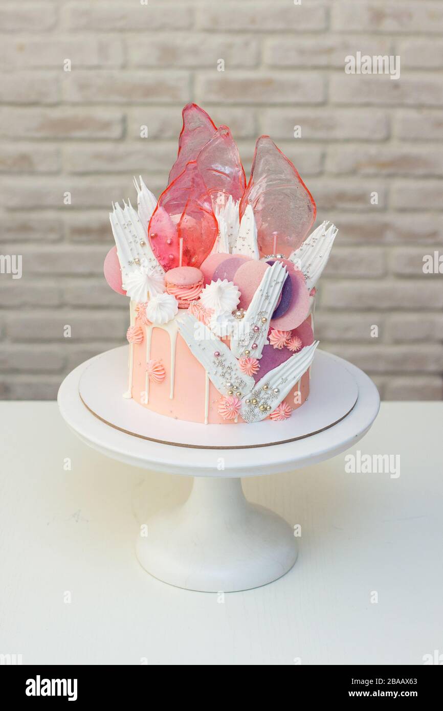 Moderna ed elegante torta rosa con caramello, cioccolato bianco, carta da waffle, meringhe e macaroon francesi decorati su cakestand bianco. Foto Stock