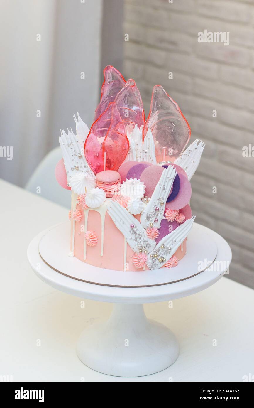 Moderna ed elegante torta rosa con caramello, cioccolato bianco, carta da waffle, meringhe e macaroon francesi decorati su cakestand bianco. Foto Stock