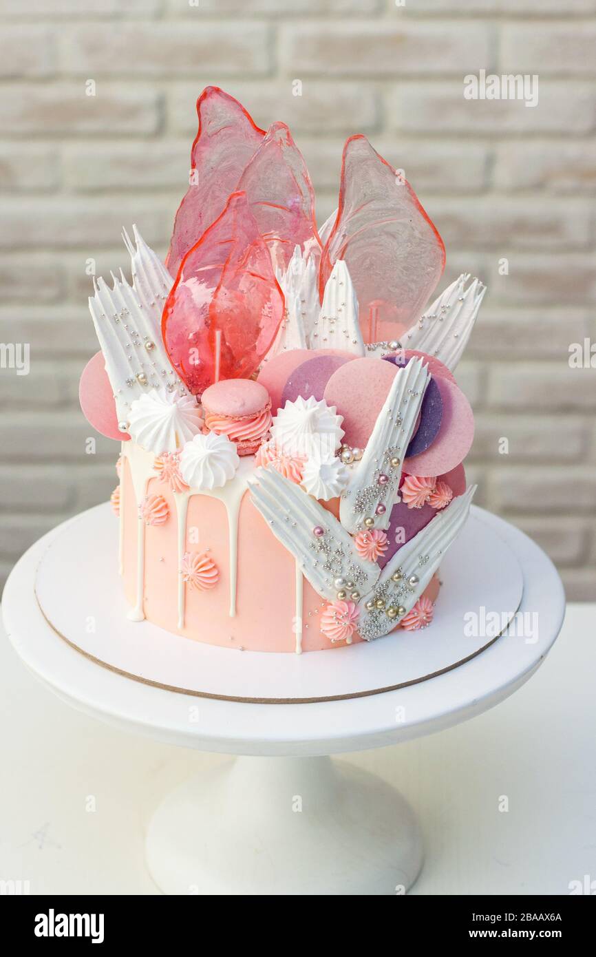 Moderna ed elegante torta rosa con caramello, cioccolato bianco, carta da waffle, meringhe e macaroon francesi decorati su cakestand bianco. Foto Stock