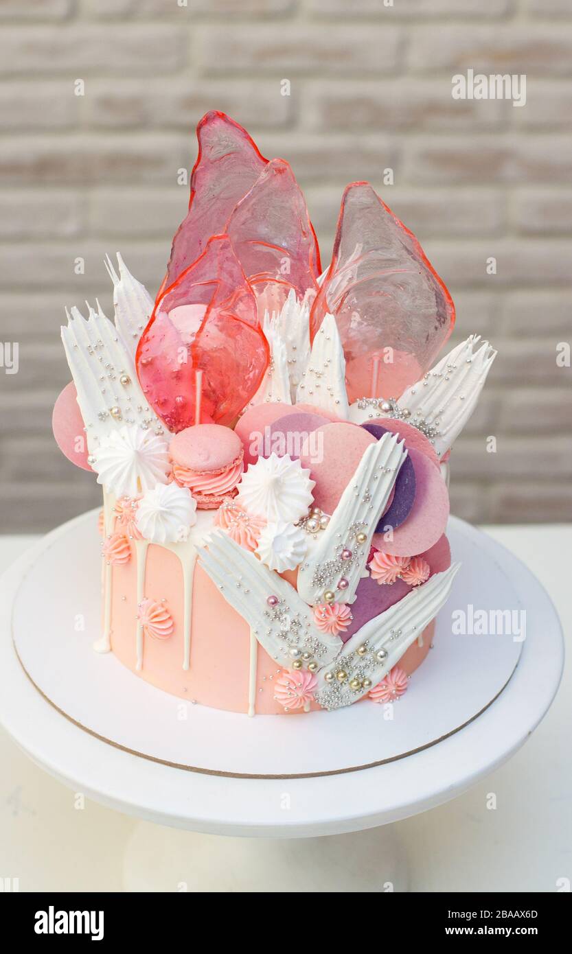 Moderna ed elegante torta rosa con caramello, cioccolato bianco, carta da waffle, meringhe e macaroon francesi decorati su cakestand bianco. Foto Stock