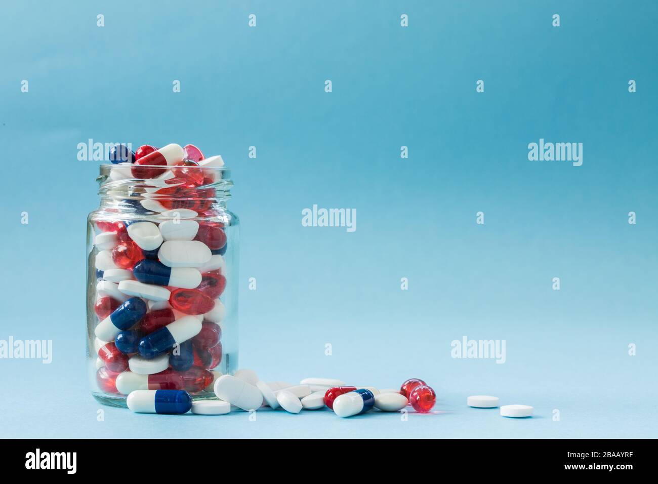 Un concetto di medicina di un vaso pieno di farmaci, compresse e pillole su uno sfondo blu con spazio di copia. Foto Stock