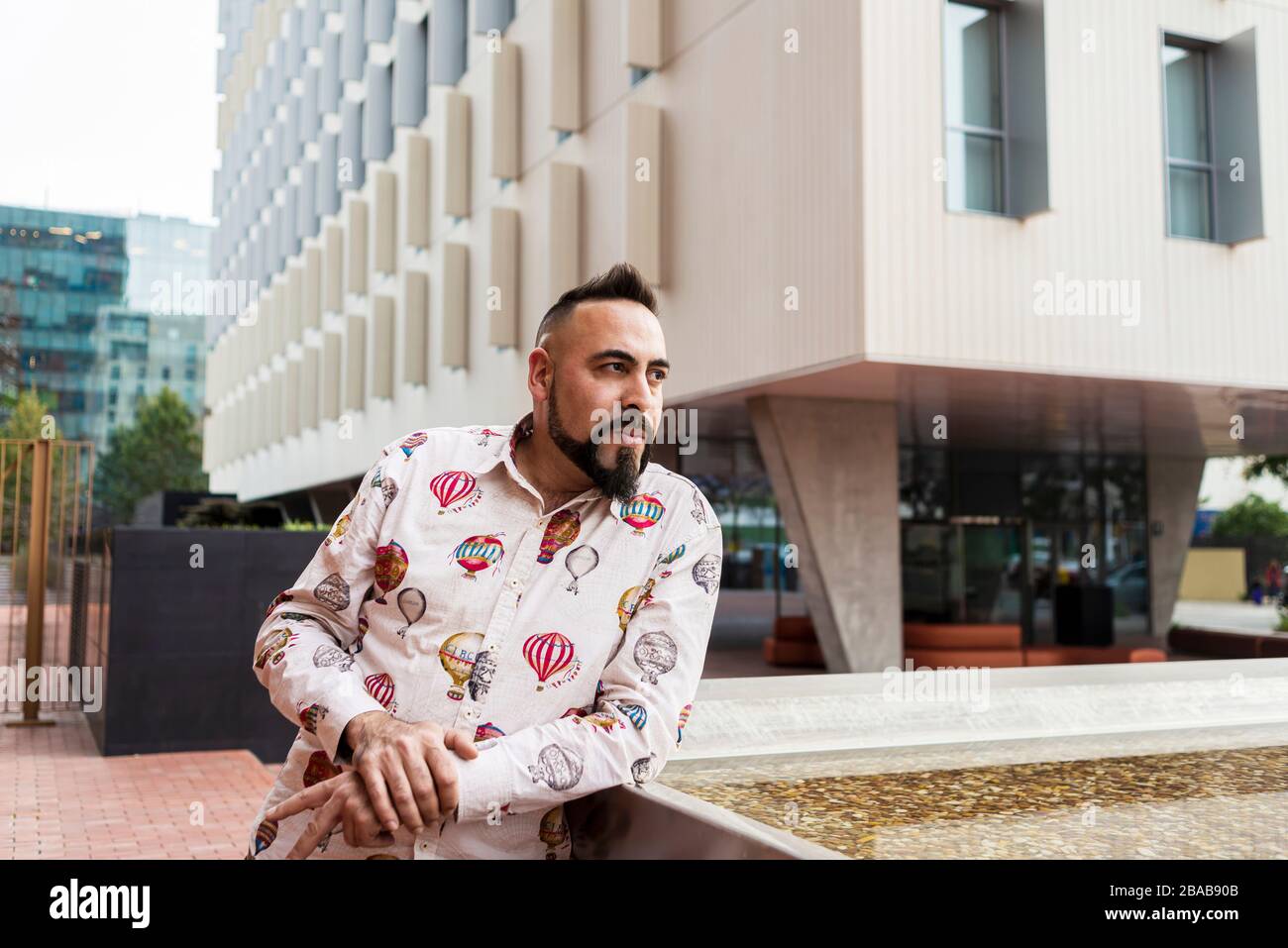 Uomo barbuto in piedi e rilassarsi sulle scale contro l'edificio degli uffici Foto Stock