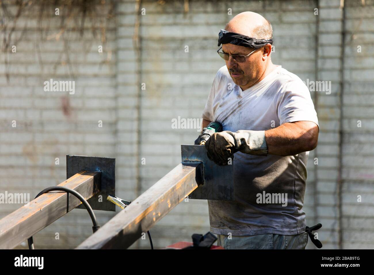 Lavoratore di metallo che fabbrica pali di metallo in officina esterna. Foto Stock