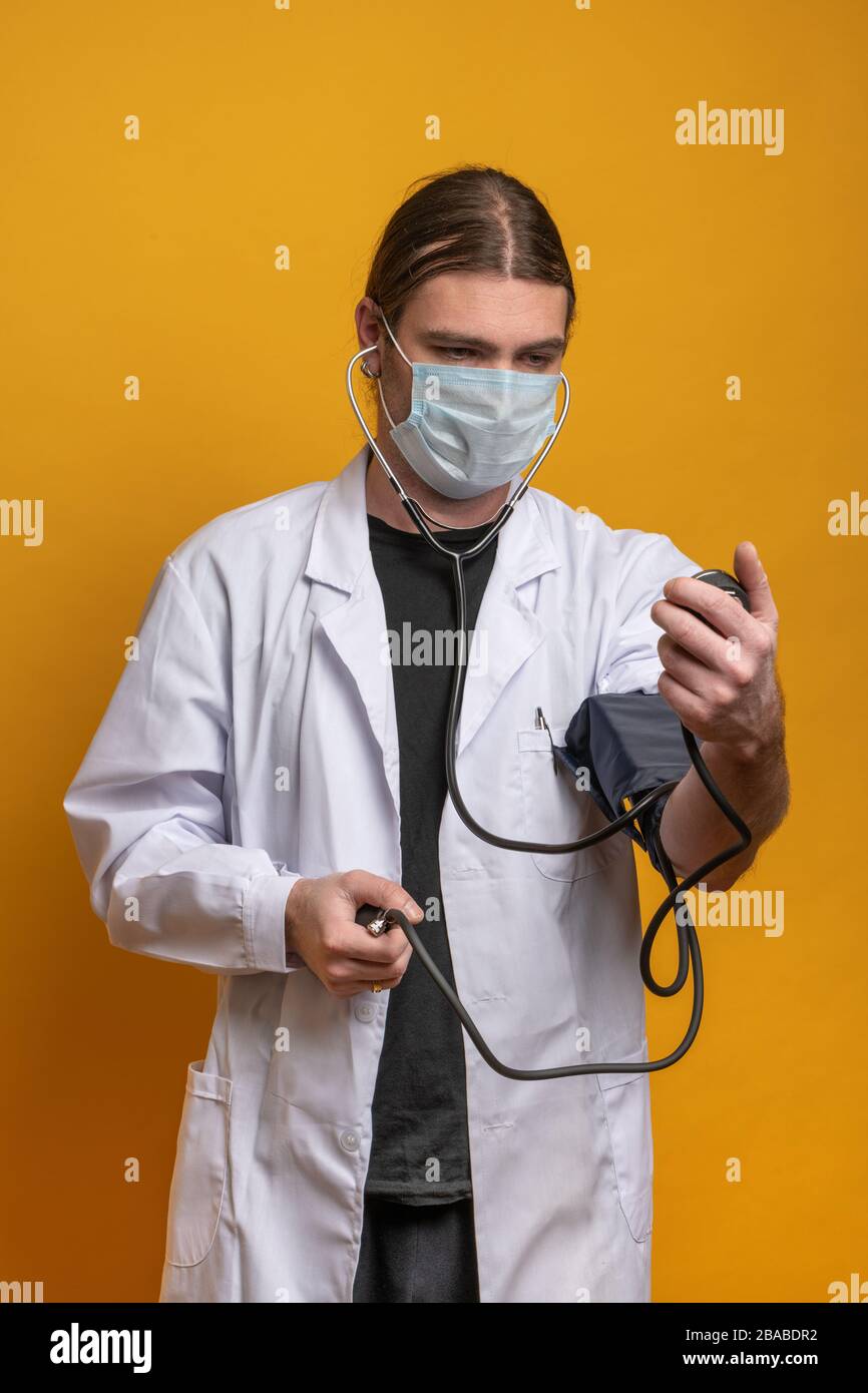 Medico giovane che misura la tensione usando un dispositivo di misurazione mentre indossa una maschera protettiva contro il virus sars-cov-2. Scatto in modalità verticale su o. Foto Stock