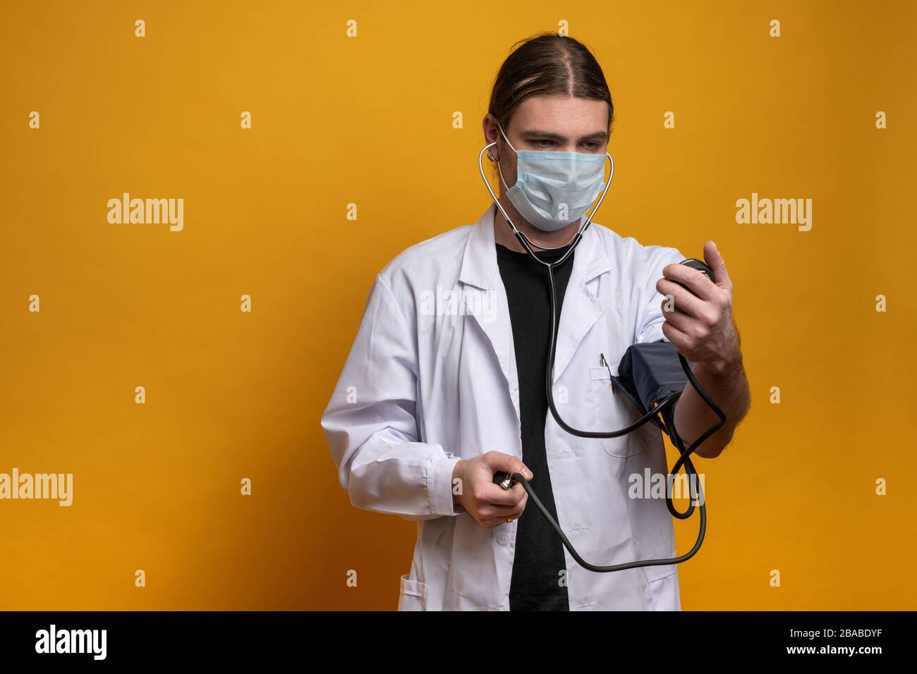 Medico giovane che misura la tensione usando un dispositivo di misurazione mentre indossa una maschera protettiva contro il virus sars-cov-2. Scatto in modalità orizzontale contro o Foto Stock