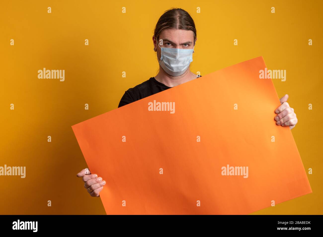 Primo piano di un giovane con maschera protettiva contro l'epidermide virale sta tenendo un cartone arancione vuoto. Spazio di copia disponibile Foto Stock