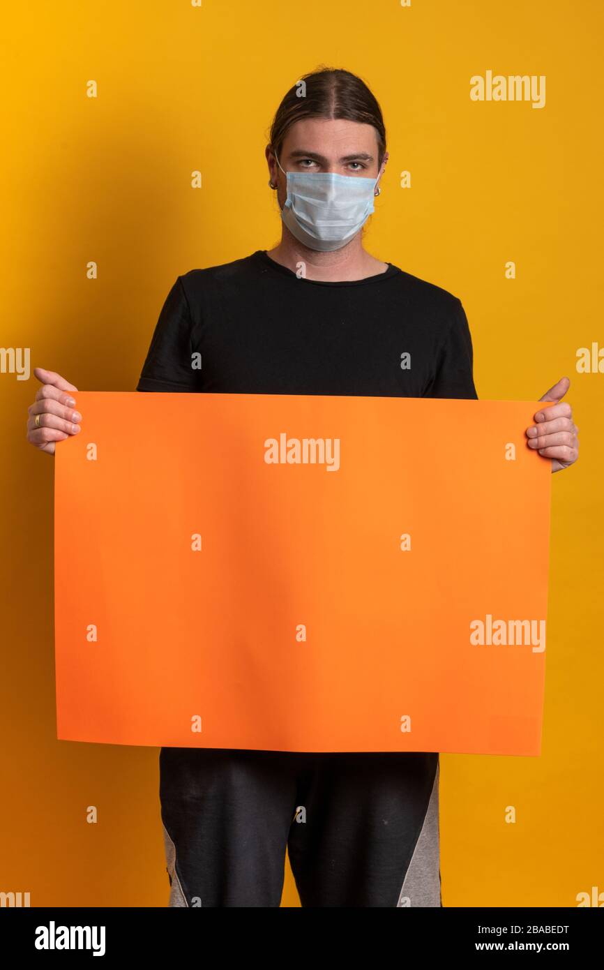 Il giovane uomo con maschera protettiva contro l'epidermide virale sta tenendo un cartone arancione vuoto. Spazio di copia disponibile Foto Stock