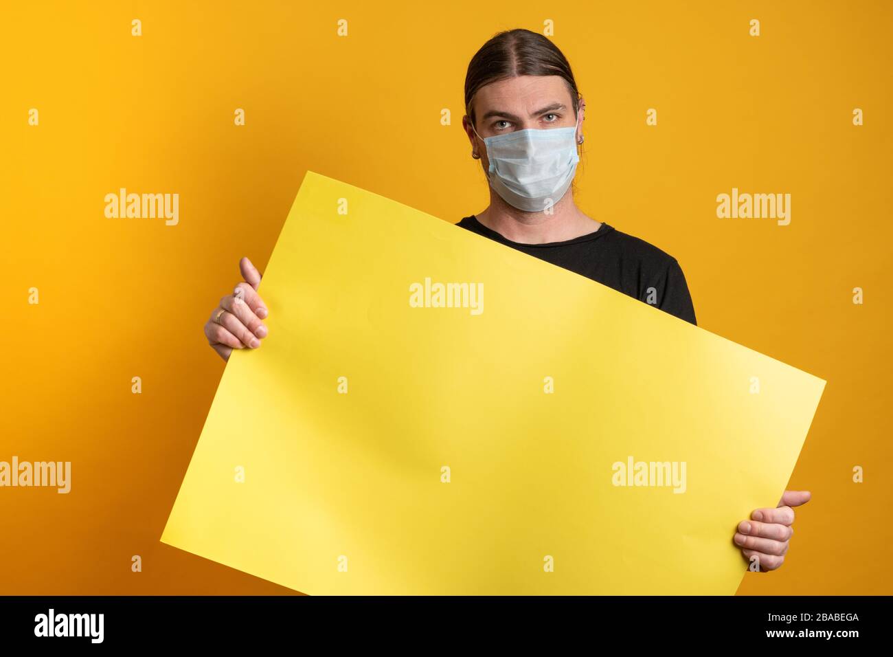 Primo piano di un giovane con maschera protettiva contro l'epidermide virale sta tenendo un cartone giallo vuoto. Spazio di copia disponibile Foto Stock