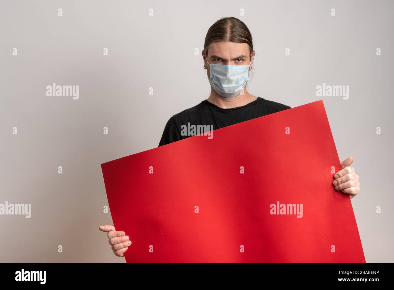Primo piano di un giovane con maschera protettiva contro l'epidermide virale sta tenendo un cartone rosso vuoto su sfondo bianco. Spazio di copia disponibile Foto Stock