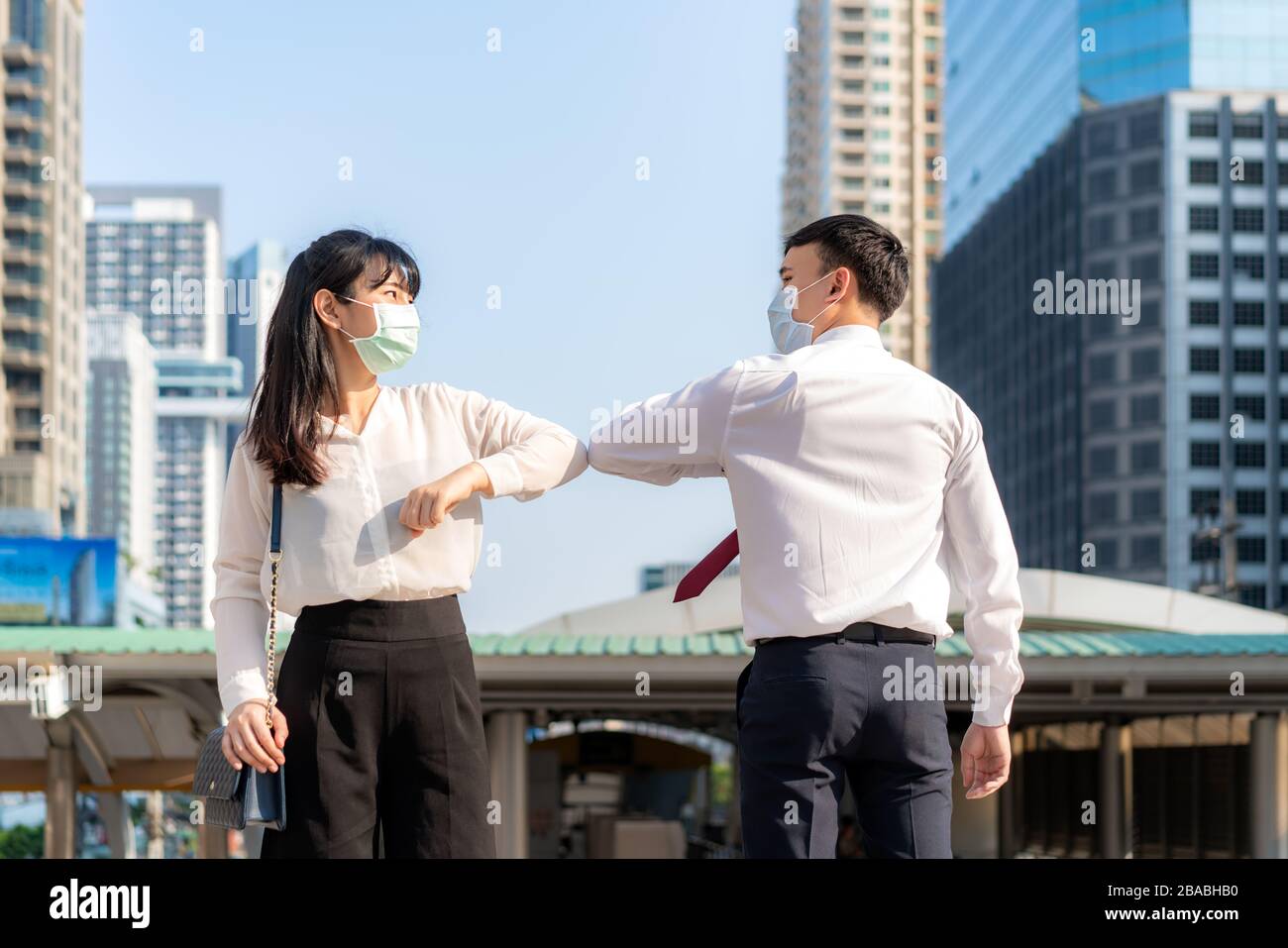 Gomito bump è nuovo saluto per evitare la diffusione di coronavirus. Due amici d'affari asiatici si incontrano di fronte all'edificio degli uffici. Invece di salutare Foto Stock
