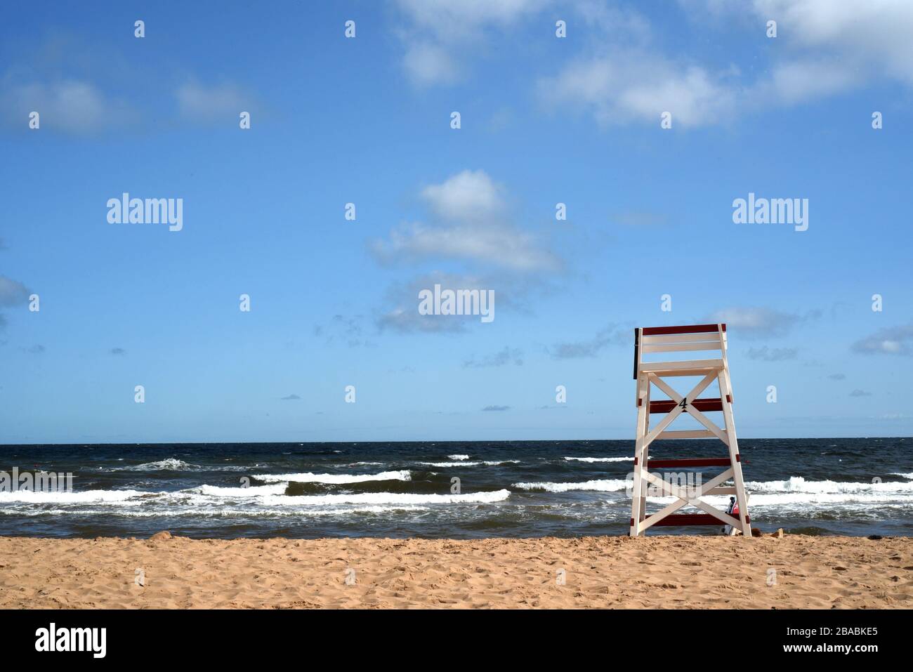 Una sedia da bagnino rossa e bianca su una spiaggia di sabbia che guarda alle onde dell'oceano e alle nuvole nel cielo blu a Cavendish Beach nell'Isola del Principe Edoardo, Foto Stock