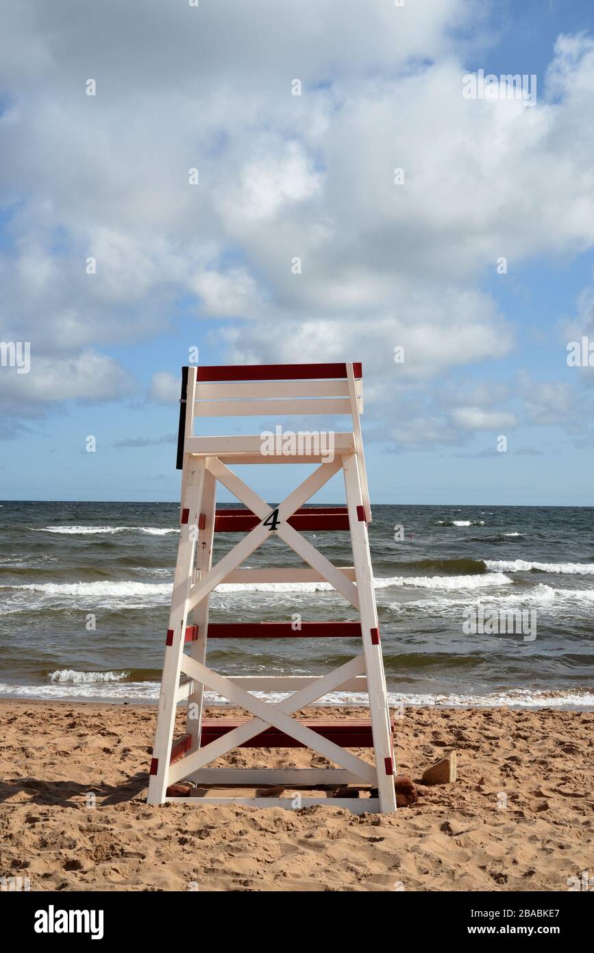 Una sedia da bagnino rossa e bianca su una spiaggia di sabbia che guarda alle onde dell'oceano e alle nuvole nel cielo blu a Cavendish Beach nell'Isola del Principe Edoardo, Foto Stock