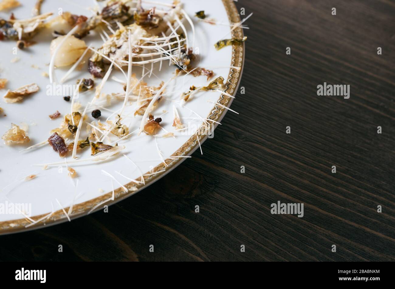 Pesce ossa su un unico piatto bianco. Sfondo tavolo in legno. Angolo di scatto con spazio di copia Foto Stock