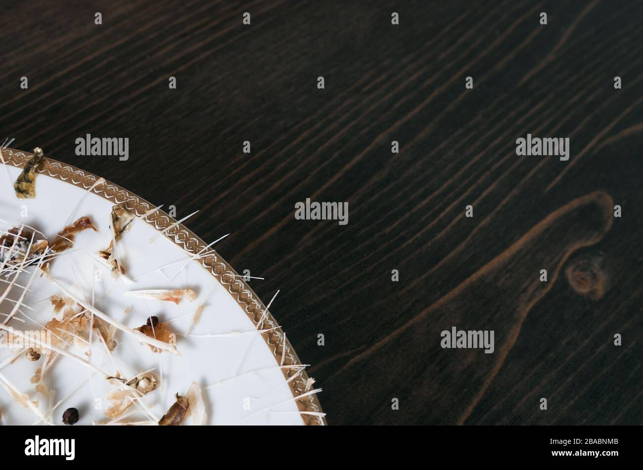 Pesce ossa su un unico piatto bianco. Sfondo tavolo in legno. Angolo di scatto con spazio di copia Foto Stock