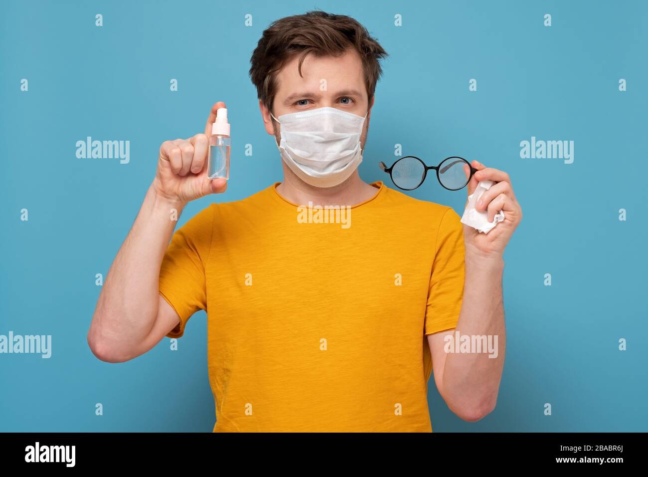 Uomo caucasico in maschera medica disinfettante gli occhiali. Precauzioni contro il coronavirus o altre infezioni. Foto Stock