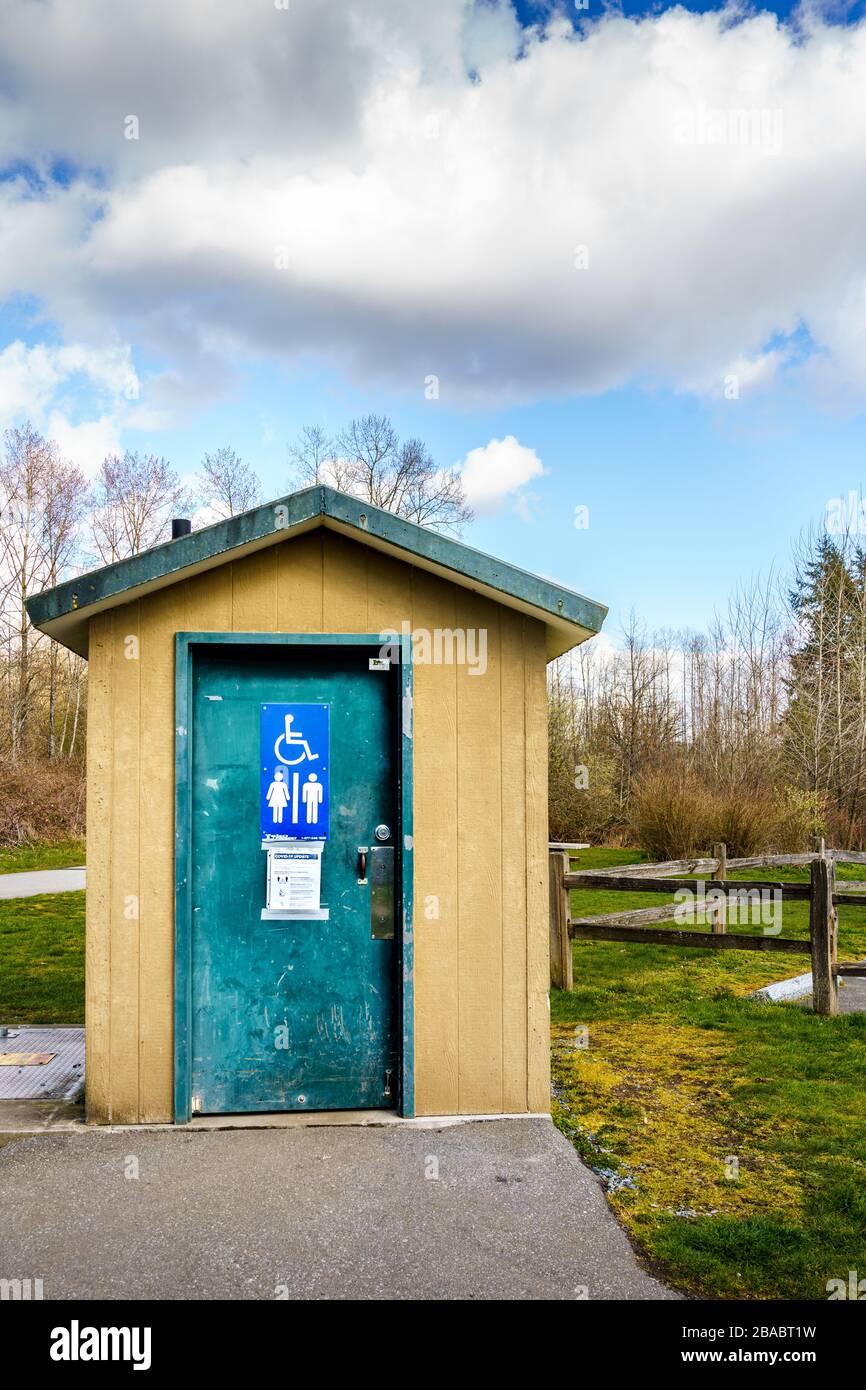 Surrey, Canada - 25 marzo 2020: toilette all'aperto al Tynehead Regional Park a Metro Vancouver con le informazioni sulla salute del virus Corona postate sulla porta Foto Stock