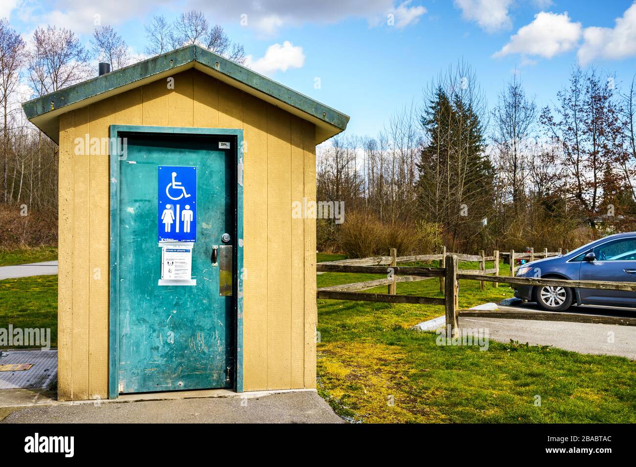 Surrey, Canada - 25 marzo 2020: toilette all'aperto al Tynehead Regional Park a Metro Vancouver con le informazioni sulla salute del virus Corona postate sulla porta Foto Stock