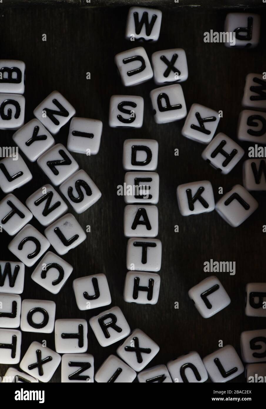 Ancora la vita che mostra blocchi di lettera in bianco e nero che ortografano la morte di parola fra altri blocchi di lettera contro uno sfondo nero Foto Stock