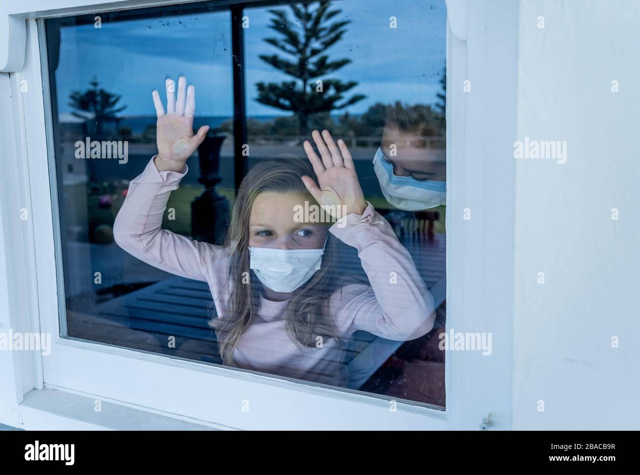 Blocco COVID-19. Bambina solitaria depressa con maschera facciale che guarda attraverso la finestra durante la quarantena. Triste bambino malato in isolamento di auto a casa. Foto Stock