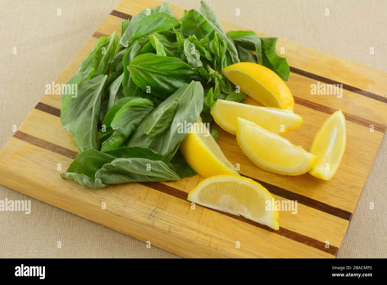 Ingredienti freschi di spicchi di limone giallo crudo e foglie di basilico fresco su tagliere di legno Foto Stock