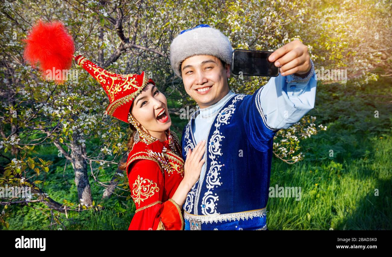 Ritratto di coppia felice in costumi kazako facendo selfie dal cellulare in fioritura primaverile apple giardino di Almaty in Kazakistan e in Asia centrale Foto Stock