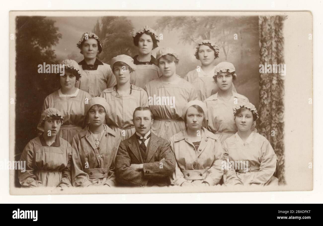 Cartolina originale studio ritratto WW1 era di gruppo di lavoratori civili munizioni femminili con manager, una delle ragazze indossa un distintivo 'on War Service', Inghilterra, Gran Bretagna, Regno Unito Circa 1916, 1917 o 1918 Foto Stock