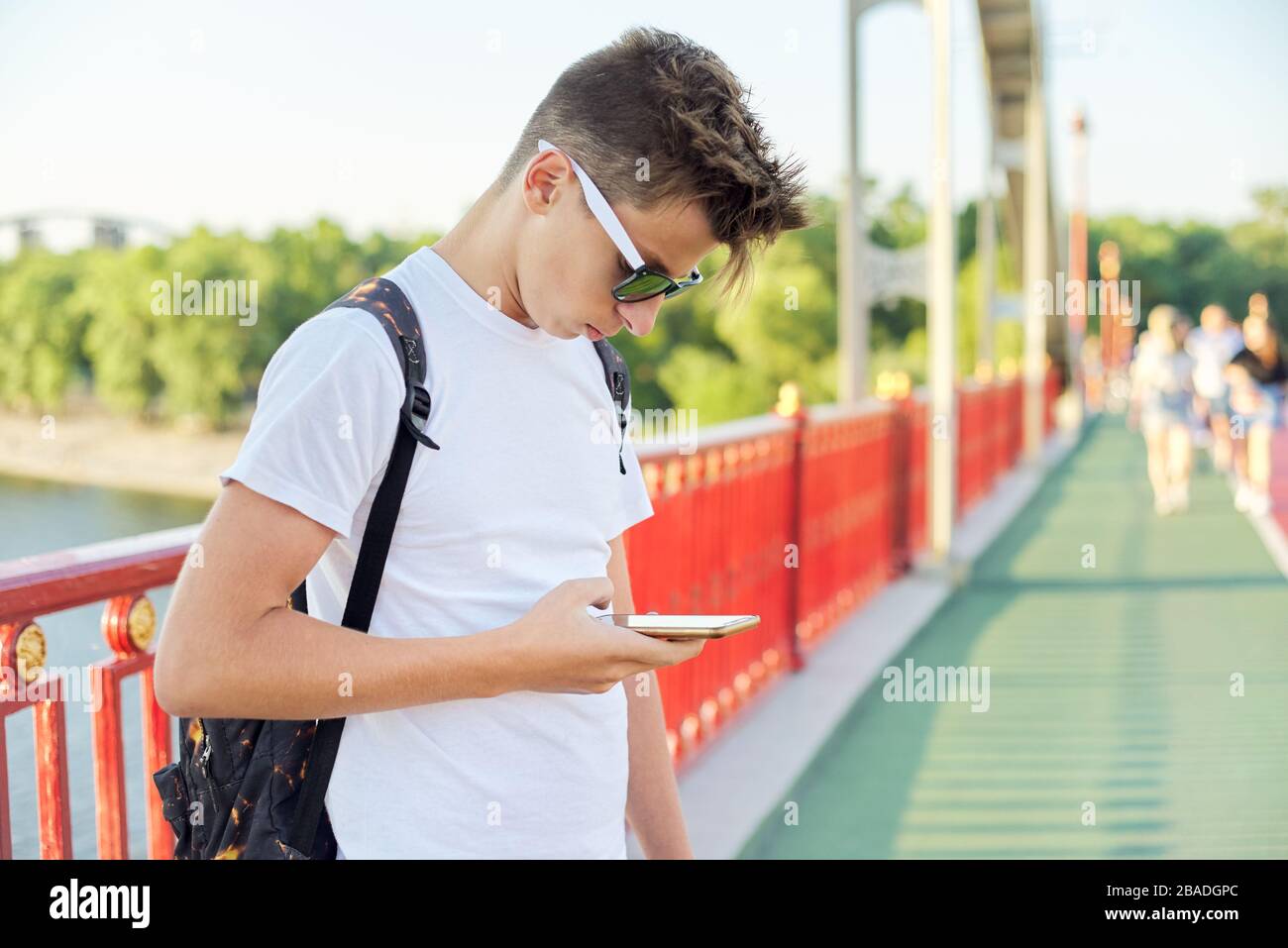 Ragazzo teen 15, 16 anni con occhiali da sole taglio moda con smartphone,  all'aperto, tramonto estate giorno sul ponte pedonale, copia spazio Foto  stock - Alamy