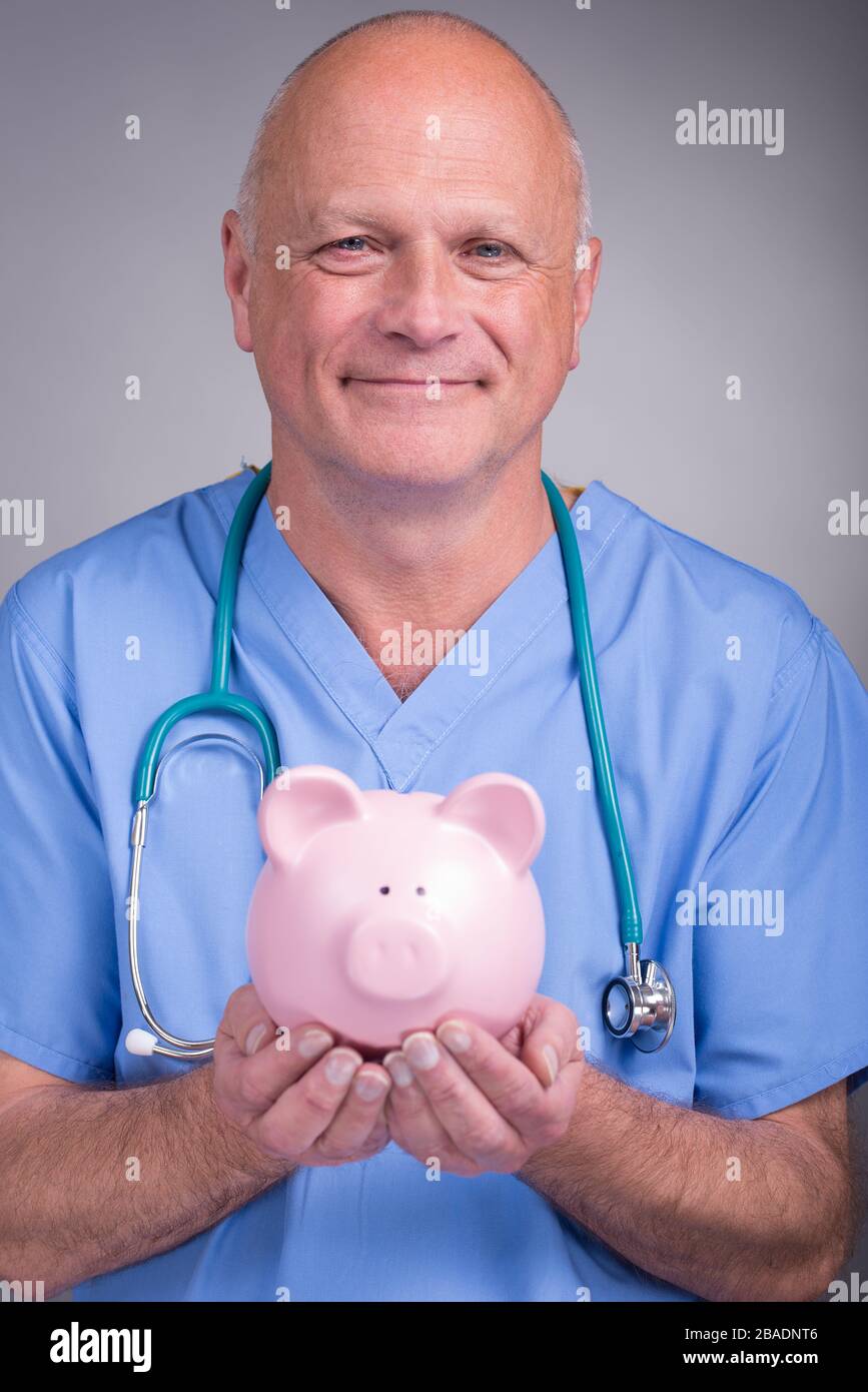 Sorridente medico che tiene una banca piggy rosa, che indossa scrub blu con stetoscopio, su uno sfondo chiaro. Foto Stock
