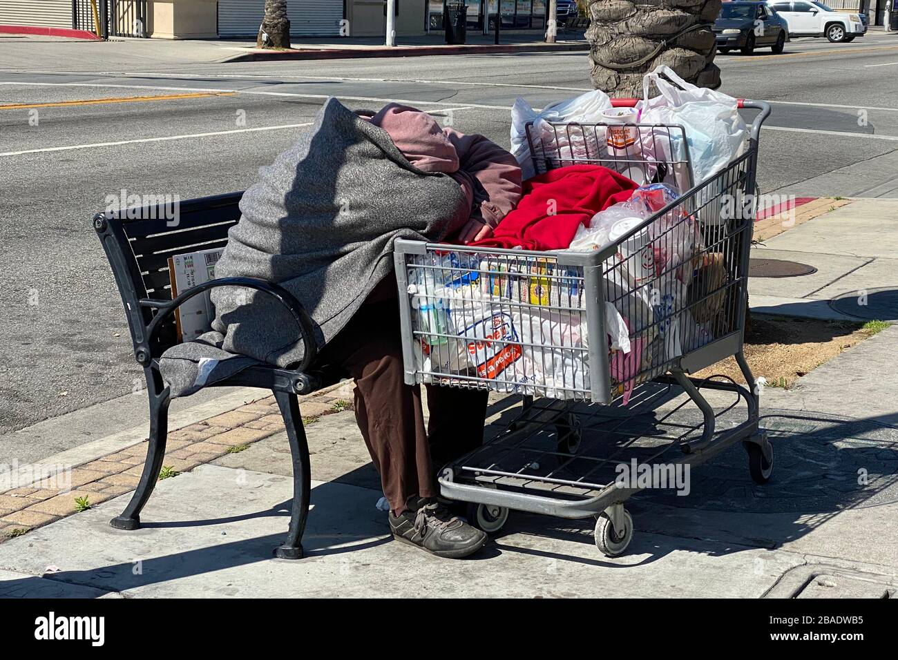 Una persona senza casa con una macchina per lo shopping siede su un banco di autobus a Whittier Blvd. In mezzo al coroinavirus globale COVID-19 epidemia pandemica, Giovedi, 26 marzo 2020, a Los Angeles. (Foto di IOS/Espa-Images) Foto Stock