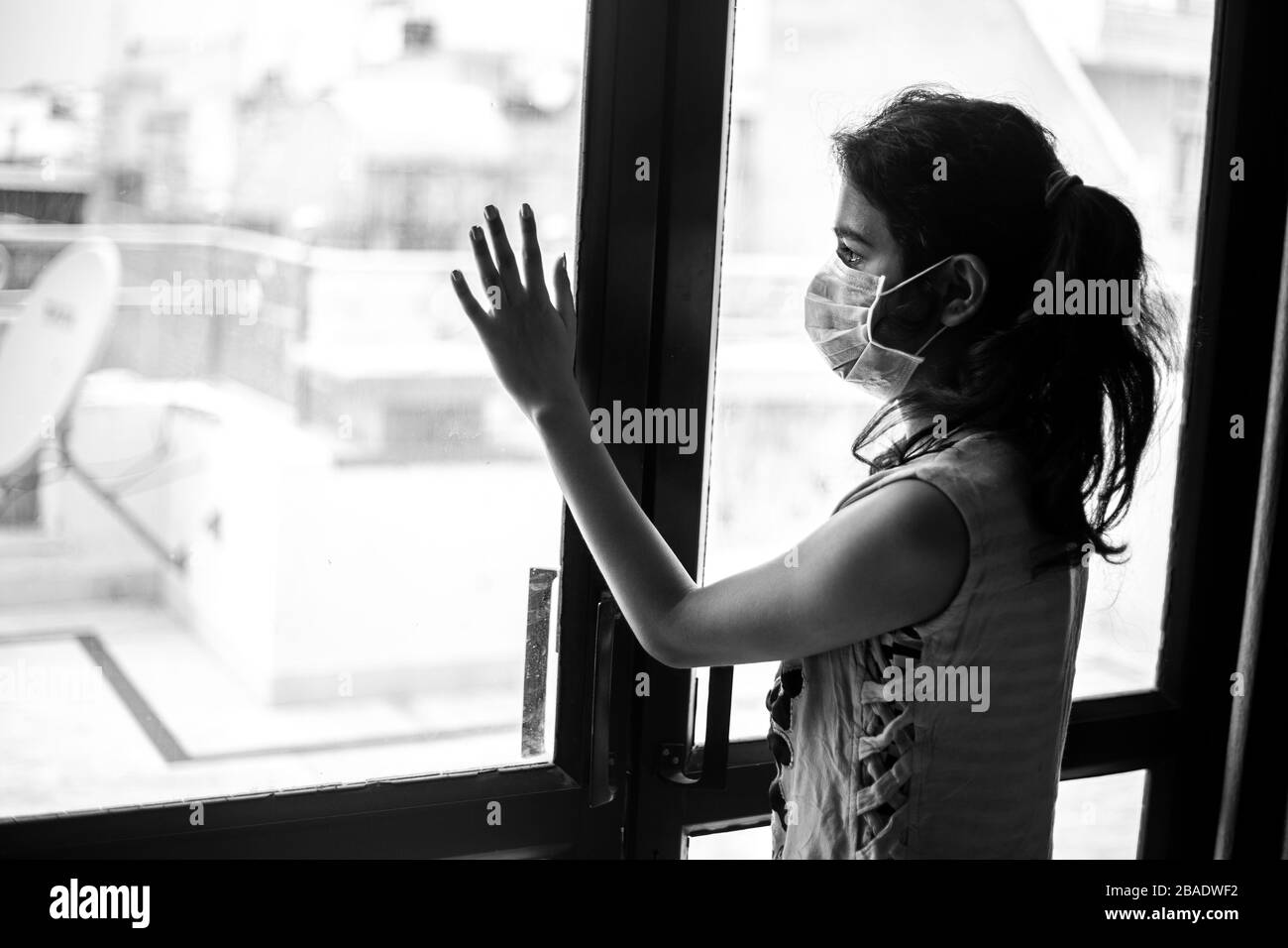 Coronavirus. Ragazza ammalata giovane di virus corona guardando attraverso la finestra e indossare maschera di protezione e recupero dalla malattia in casa. Quarantena. Foto Stock