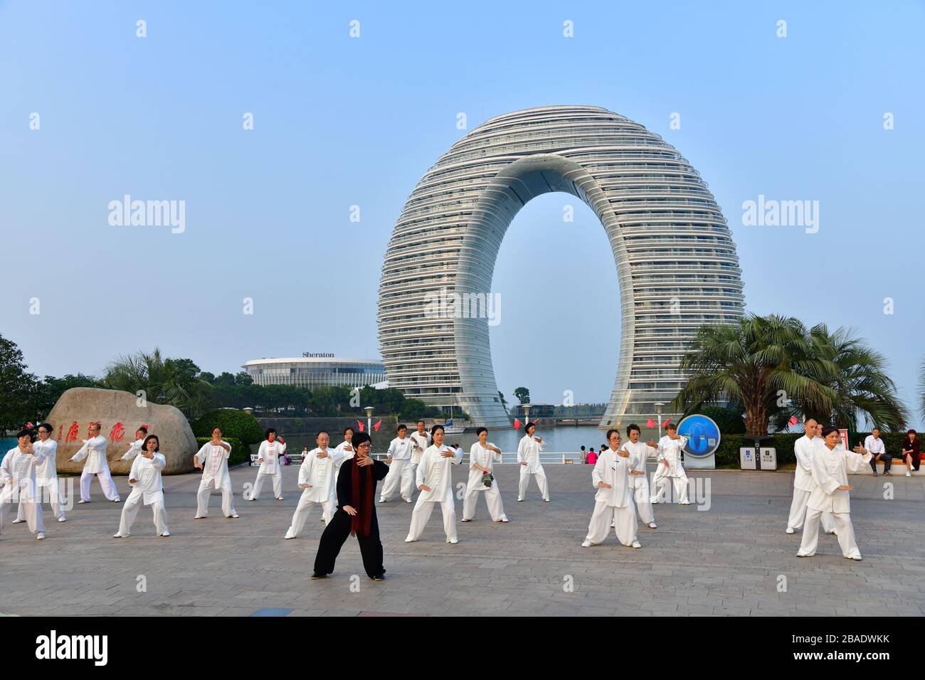 Huzhou, Cina, ottobre 2019; un grande gruppo di persone che praticano Tai Chi, in stile Yang, sulle rive del lago Tai con l'iconico hotel a forma di ferro di cavallo Foto Stock