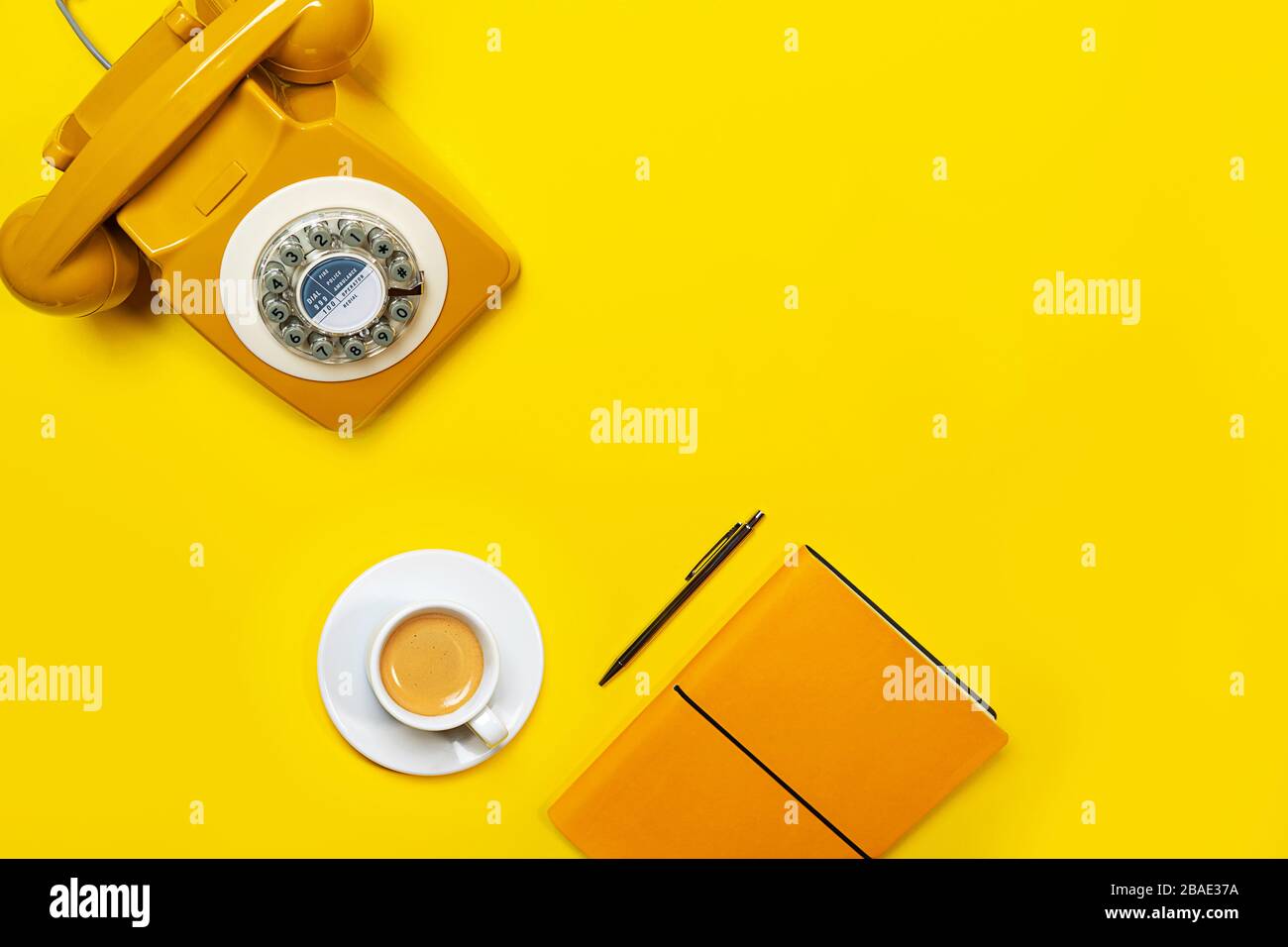 Disposizione gialla con telefono retrò rotante, tazza di caffè, penna e notebook. Disposizione piatta, vista dall'alto, spazio copia. Foto Stock