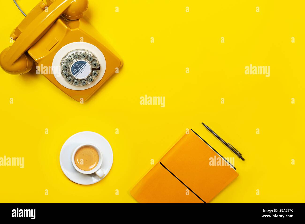 Disposizione gialla con telefono retrò rotante, tazza di caffè, penna e notebook. Disposizione piatta, vista dall'alto, spazio copia. Foto Stock