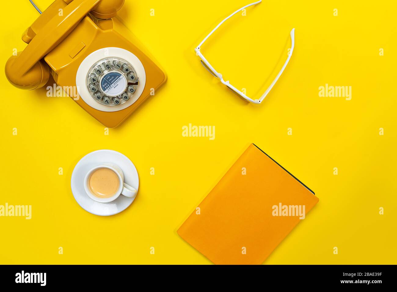 Disposizione gialla con telefono retrò rotante, tazza di caffè, occhiali da sole e notebook. Disposizione piatta, vista dall'alto, spazio copia. Foto Stock