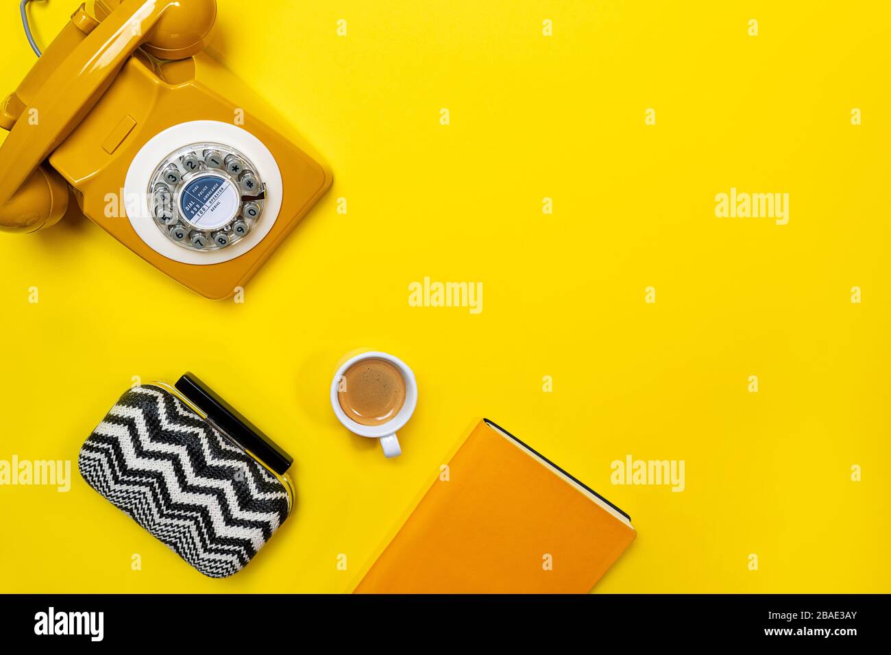 Disposizione gialla con telefono retrò rotante, tazza di caffè, borsa e notebook. Disposizione piatta, vista dall'alto, spazio copia. Foto Stock