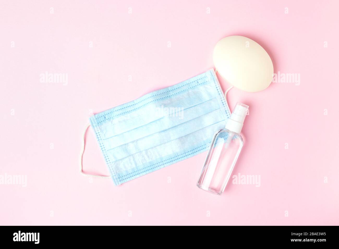 Maschera medica blu, sapone e antisettico su sfondo rosa. Protezione contro i virus. Foto Stock