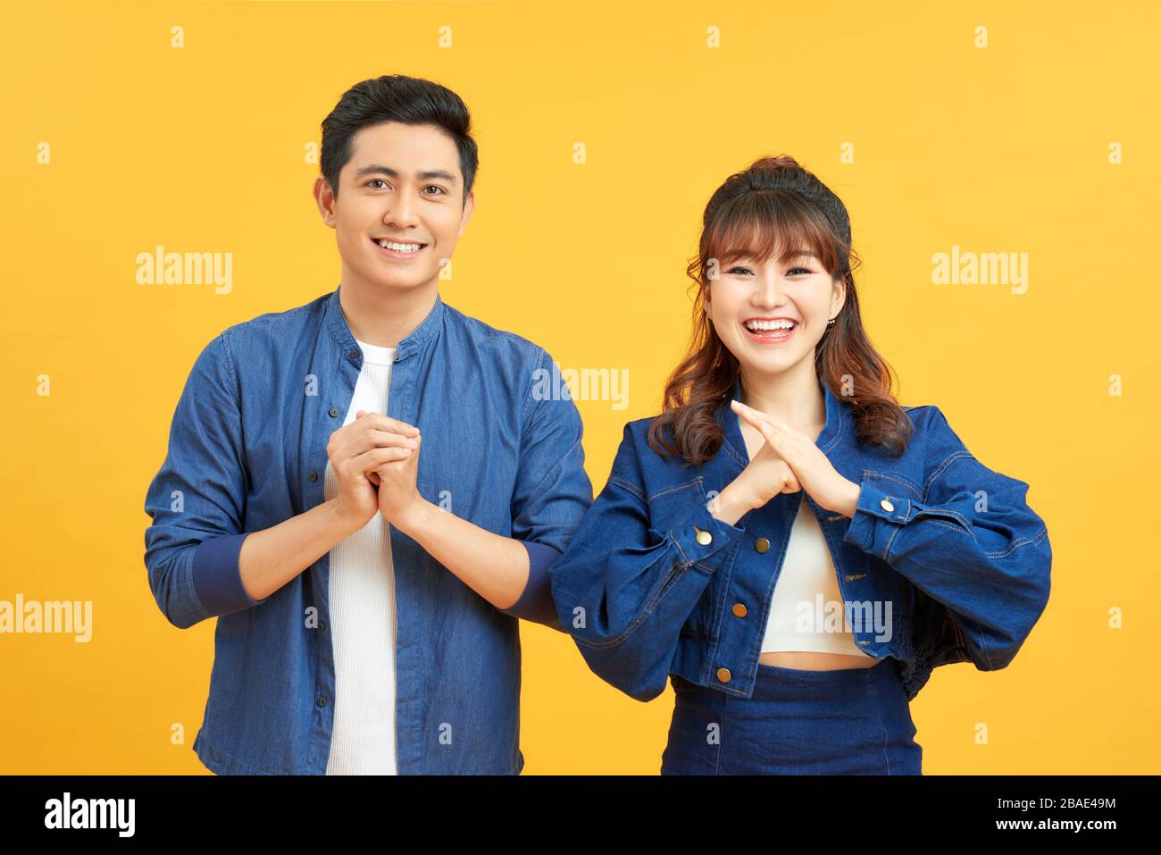 Giovane coppia che si posa in uno sfondo giallo stringendo le mani alla fotocamera in gesto congratulazioni. Foto Stock
