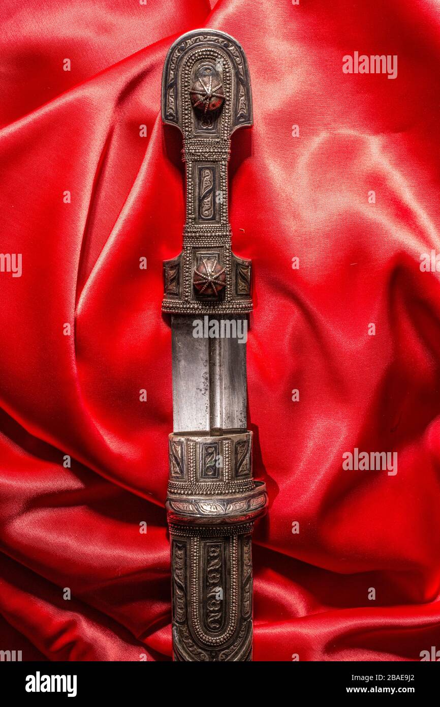 Bell'esempio di pugnale caucasico con lama a forma di spada di Roma su sfondo di seta rossa. 19th secolo (tempo delle guerre russo-caucasiche (1816-1864 Foto Stock