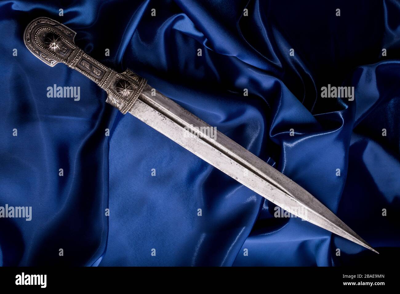 Bell'esempio di pugnale caucasico con lama a forma di spada di Roma su sfondo di seta blu. 19th secolo (tempo delle guerre russo-caucasiche (1816-186 Foto Stock