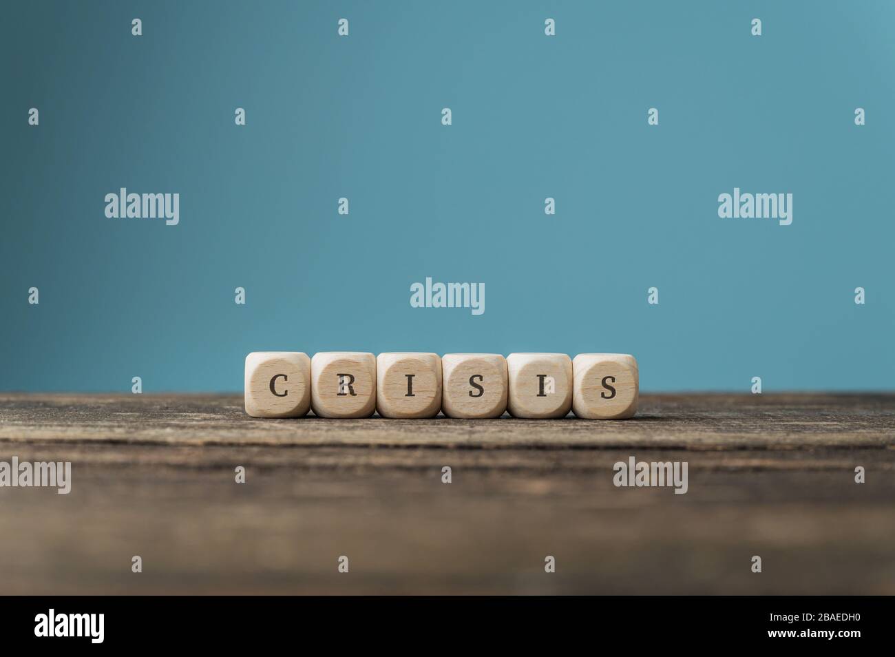 Word Crisis scritto su dici di legno posto su una scrivania su sfondo blu. Foto Stock