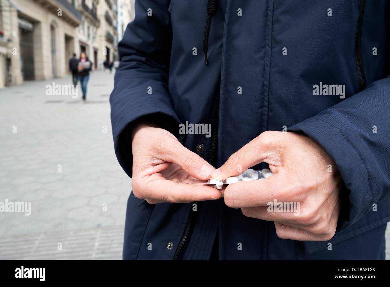 primo piano di un uomo caucasico per strada, con un parka blu, ottenendo una pillola da una confezione blister Foto Stock
